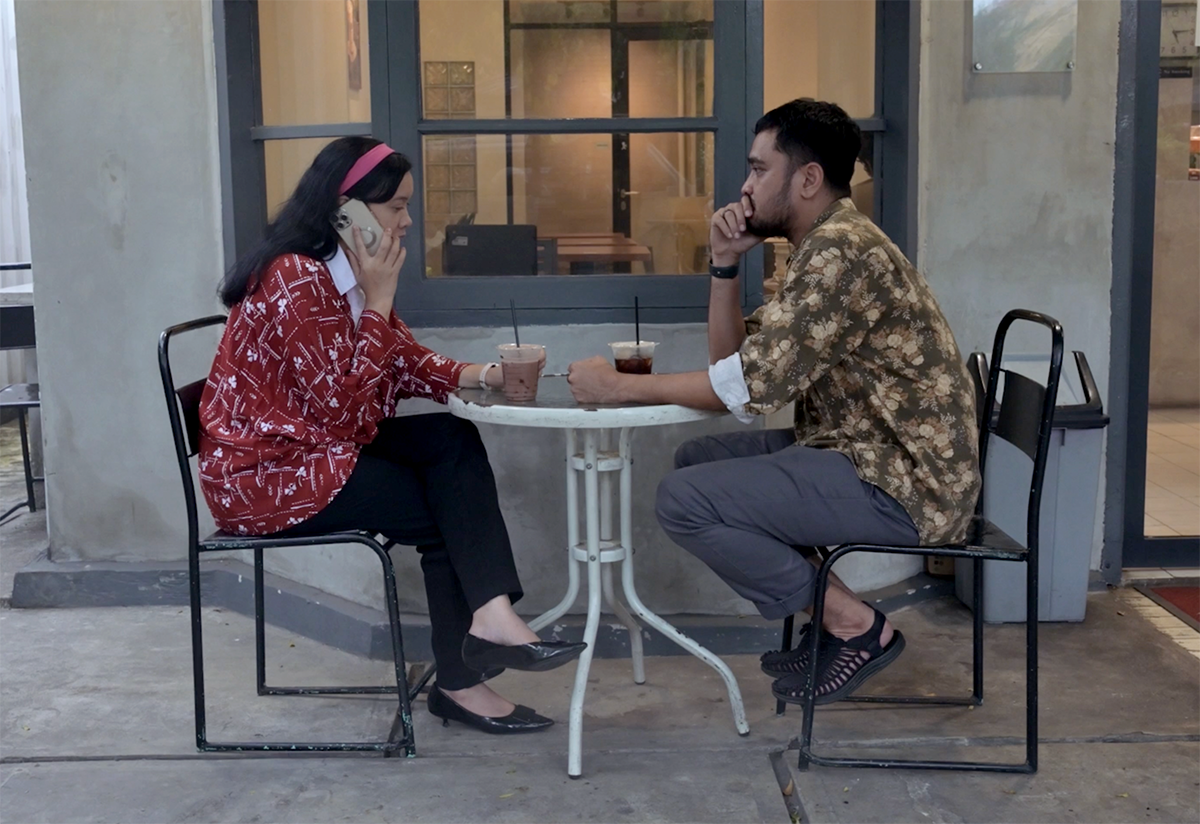 Ridhwan Siregar dan Kiki Siregar duduk di meja kafe, menelepon saat persiapan wawancara.